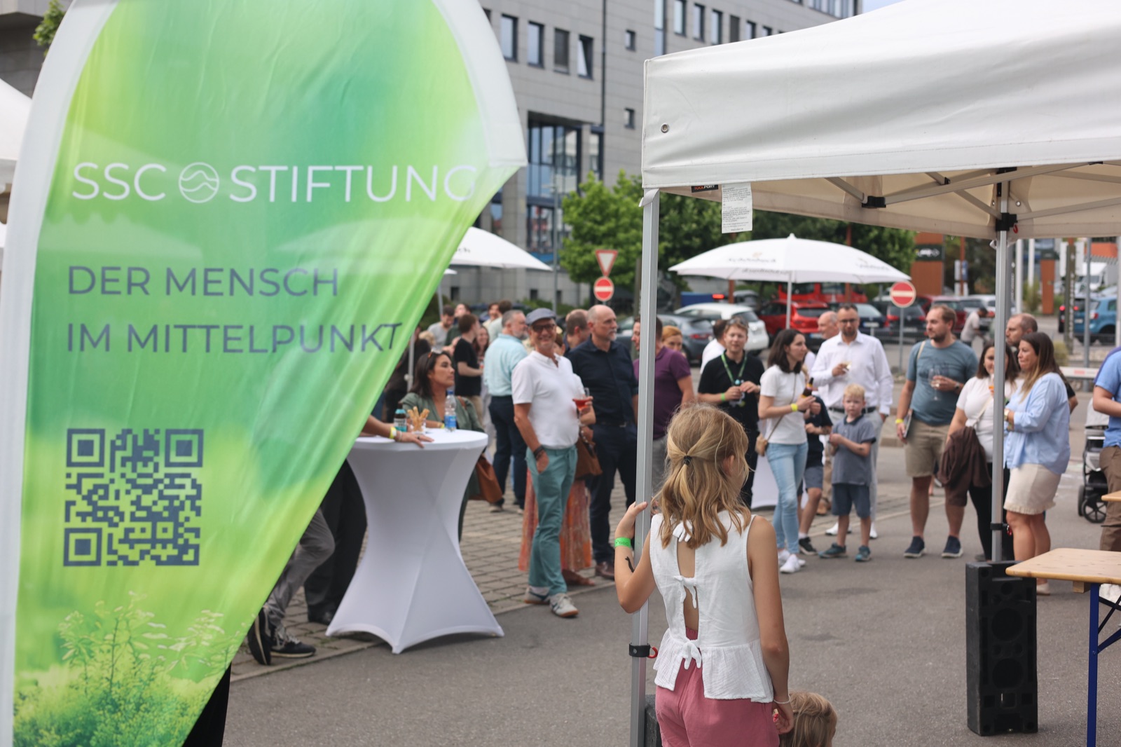Gäste des SSC-Sommerfests neben der Fahne der SSC Stiftung mit dem Motto „Der Mensch im Mittelpunkt“